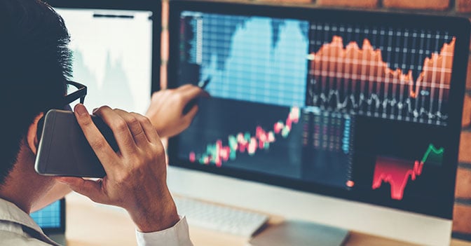 Business man on phone looking at graph on computer monitor